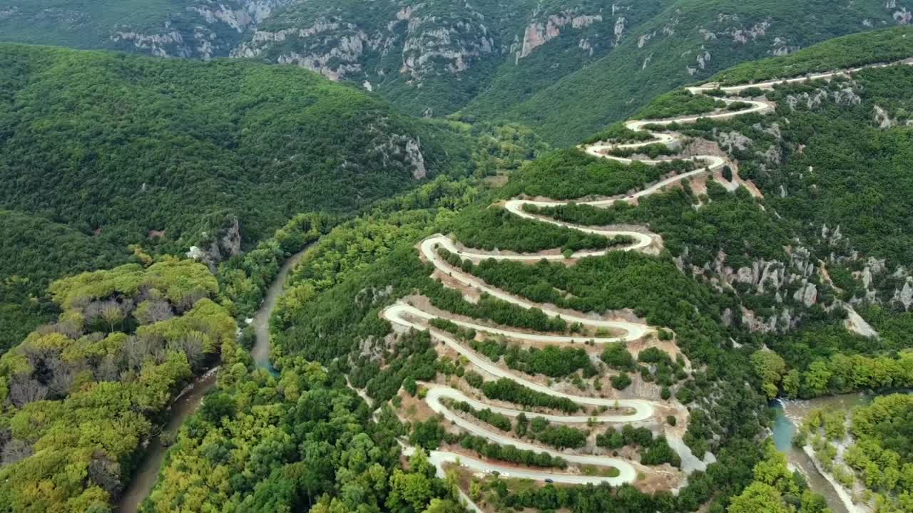 Kinoreifes Drohnenpanorama der berühmten Serpentinen in Papigo. Hochwinkelaufnahme, die die Zickzack-Bergstraße zeigt, eingebettet zwischen den üppigen Ufern des Voidomatis-Flusses in Epirus. Ideal für Reiseinhalte.