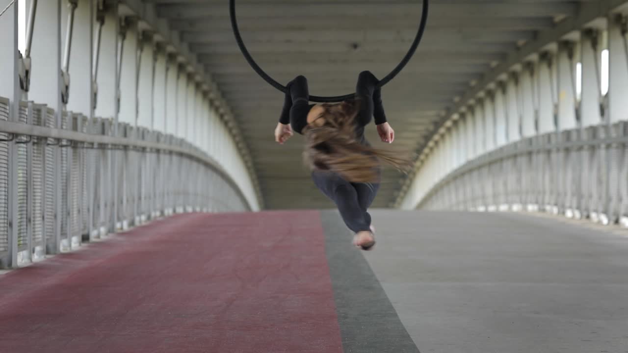 Woman performing acrobatic stunts on an aerial hoop in an urban bridge