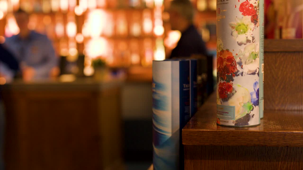 Warmly lit distillery bar with people browsing whiskey bottles, shallow focus, slow camera pan