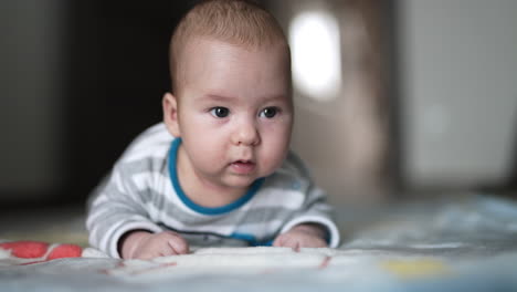 baby boy in striped shirt struggling to hold his head up. lovely kid with plump cheeks close up. blurred backdrop.
