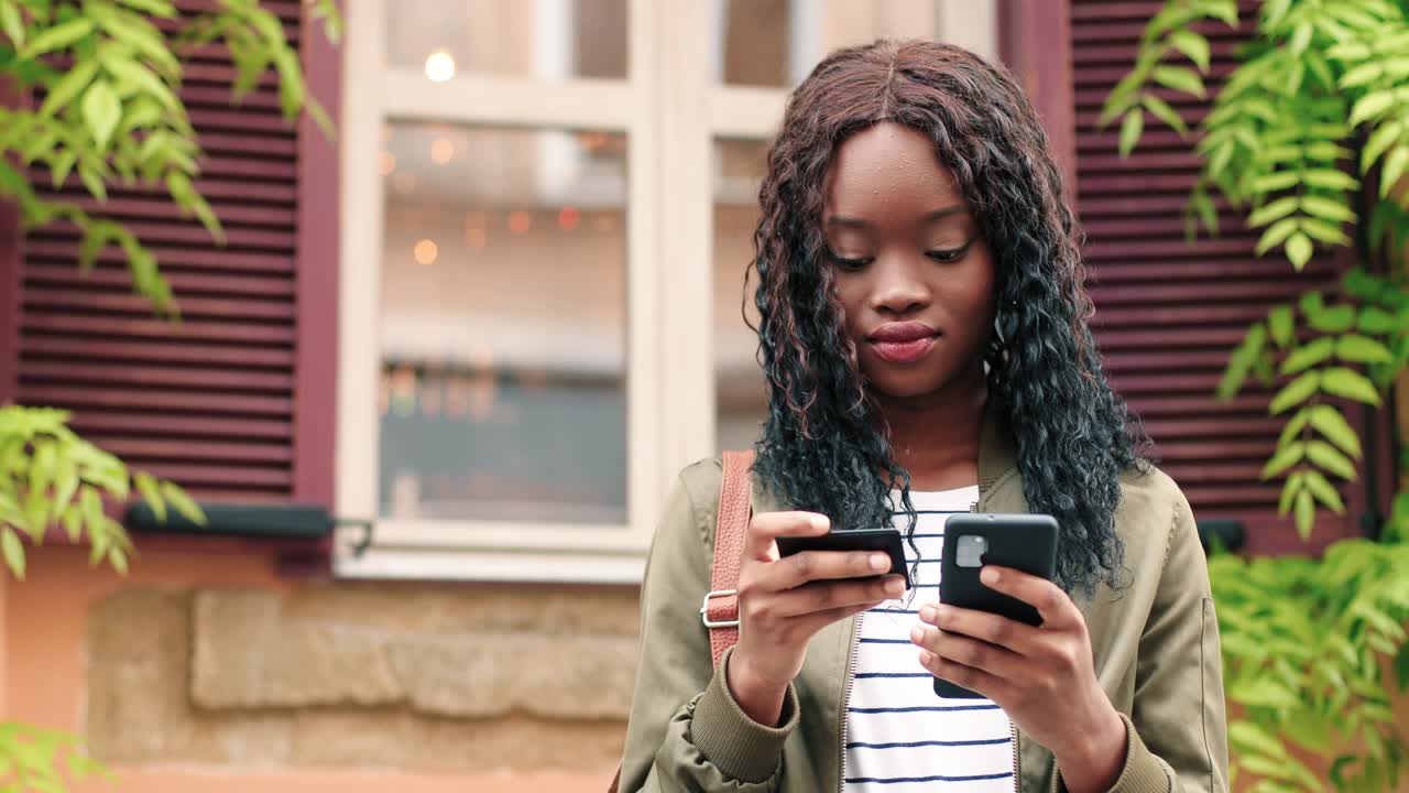 Afroamerikansk kvinde handler online med smartphone på gaden, hvorefter hun fejrer og smiler