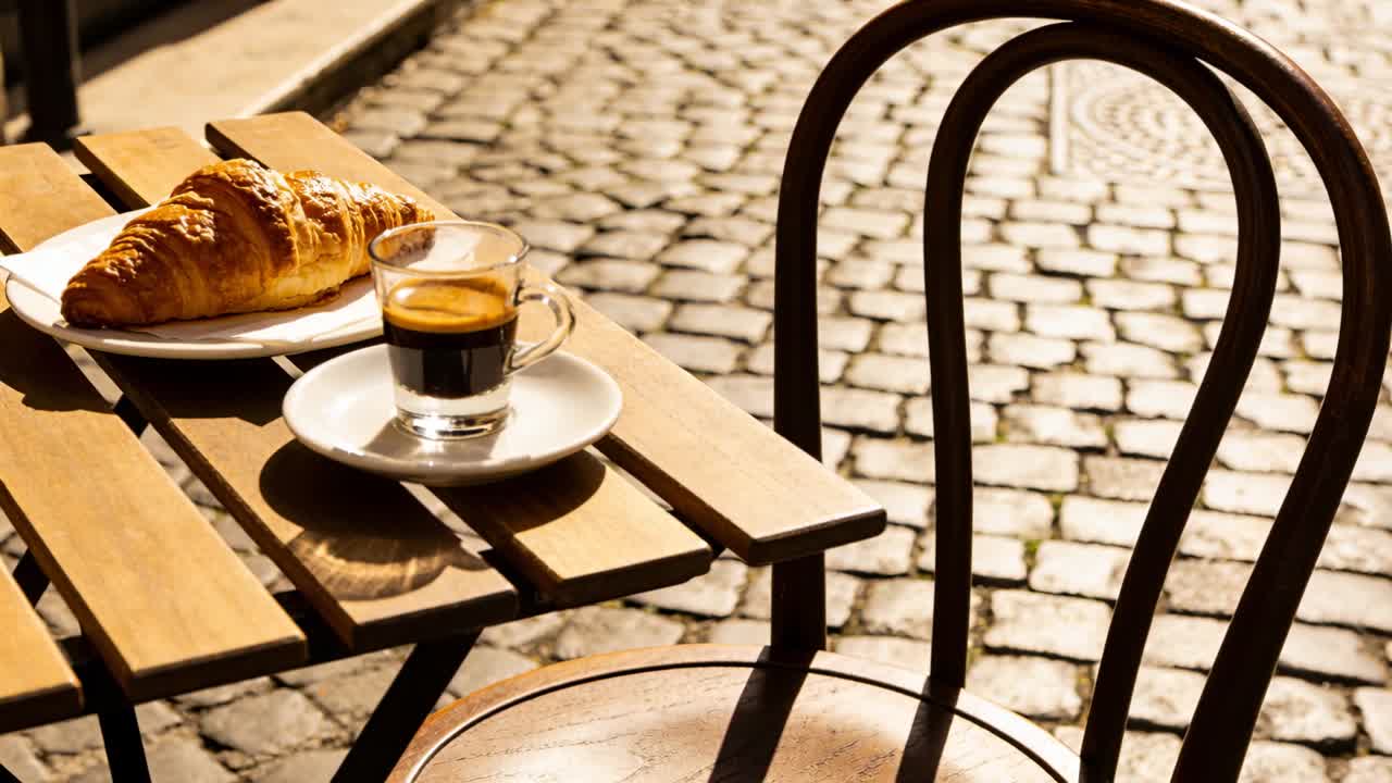 Sol em movimento projetando sombras sobre mesa de madeira de café de rua com croissant e xícara de café expresso