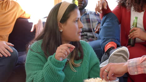 amigos varones y mujeres felices hablando en casa, bebiendo cervezas y comiendo palomitas de maíz