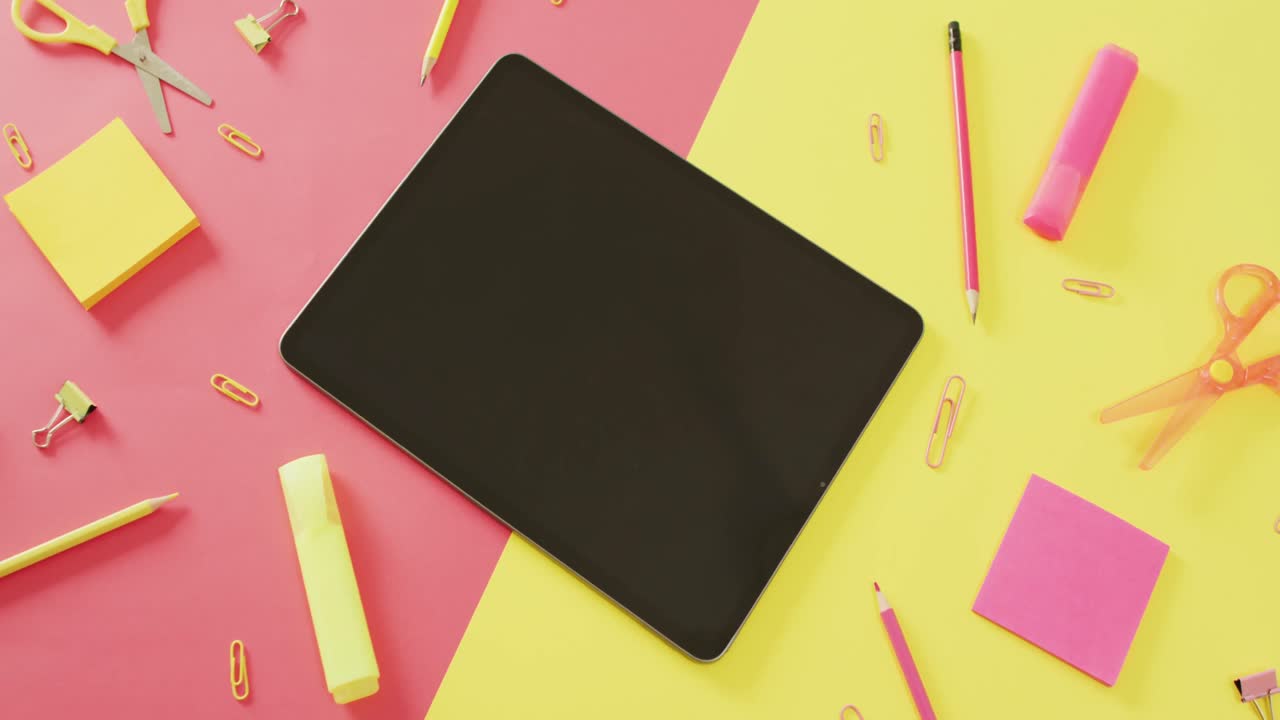 vídeo de una tableta con espacio para copiar y artículos escolares en superficie rosa y amarilla
