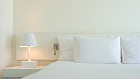 tilt down on a modern hotel room made in white colors - bed with a set of four pillows and turned on night lap landing on cabinet