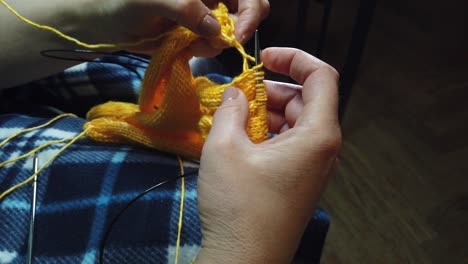 women's hands knit woolen jacket with knitting needles. top view, close-up of hands and knitting.