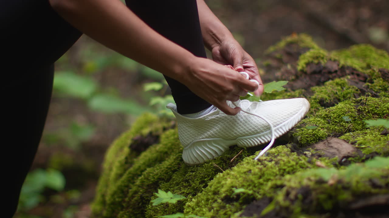 Woman tying shoelaces on white sneakers in a forest