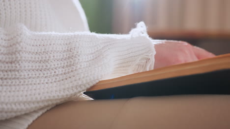 close view of female hands flipping through pages of textbook while seated in soft natural light, highlighting tactile interaction with paper, warm ambient setting with cozy outfit