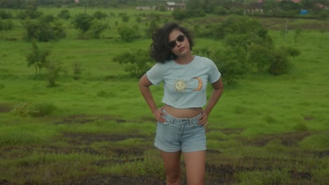 An-Indian-young-woman-with-stylish-sunglasses,-playfully-runs-her-fingers-through-her-hair-in-the-midst-of-the-serene-and-natural-environment