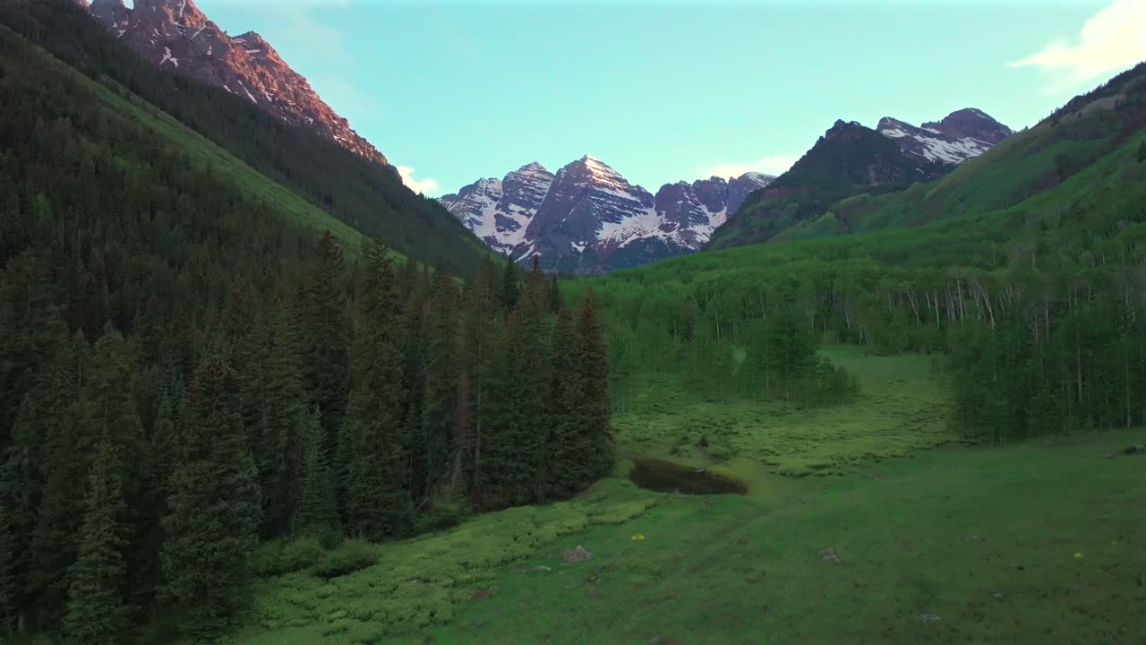 Maroon Bells North Maroon Wilderness valley aerial drone Colorado Elk Range Rocky Mountains spring summer golden sunset blue sky clouds Aspen Snowmass White River National Forest forward motion
