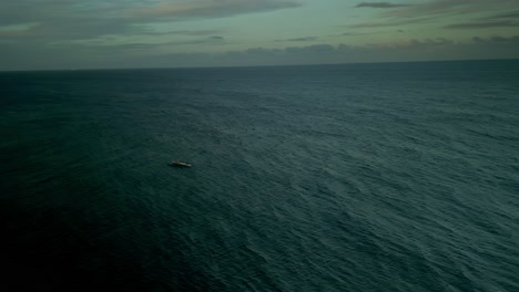 Lone-small-boat-on-wavy-blue-open-sea-on-cloudy-day,-wide-aerial-pan