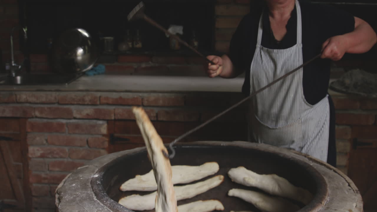 anciana panadera sosteniendo un palo de hierro, sacando el pan shoti recién horneado de un horno de arcilla redondo