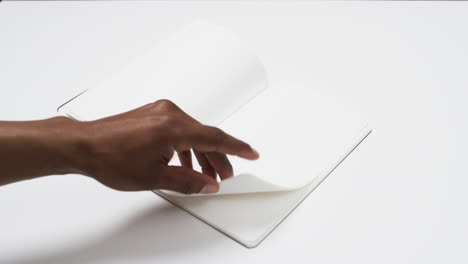 Video-of-hand-of-african-american-man-holding-book-with-blank-page,-copy-space-on-white-background