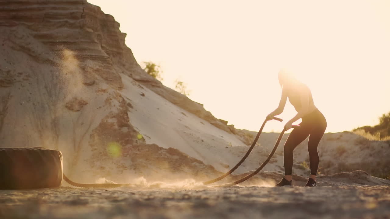 해가 지는 동안 모래 언덕 주변에서 야외 훈련을 하는 여성 운동 선수. 적극적인 신체 활동 운동. 크로스피트