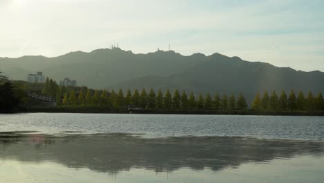 lago tranquilo en el gran parque de seúl bajo el brillante cielo nublado durante el otoño rodeado de árboles verdes y altas montañas - disparo de gran angular