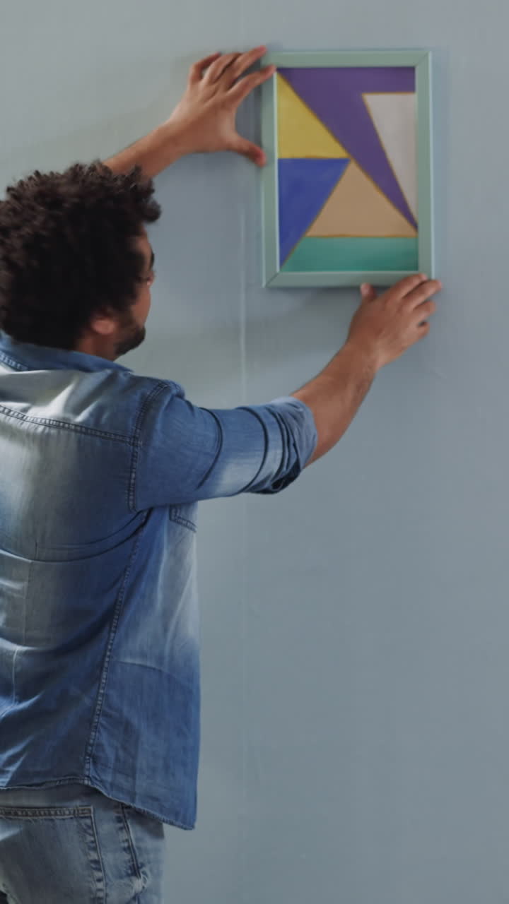 African-America men hang abstract drawing straight on wall in studio backside view. Art object for interior design trends. Work upon domestic style