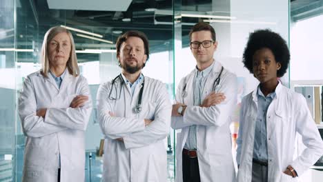 multiethnic doctors team in white coats looking at camera in good mood while standing in hospital corridor