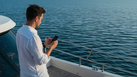 serene moment at sea: a man engaged with his smartphone on a yacht, enjoying tranquil waters and the warm glow of the setting sun