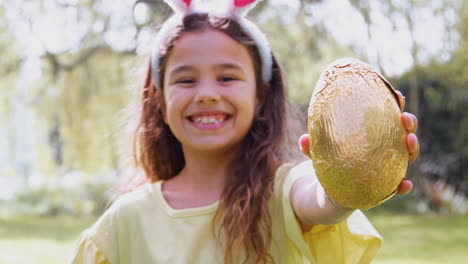 retrato de una niña con orejas de conejo sosteniendo un huevo de chocolate en la caza de huevos de pascua en el jardín