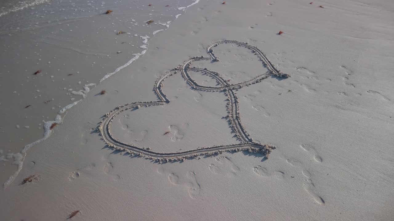 Angled shot of two interlocking hearts inscribed in the sand on a beach