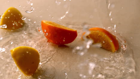 trozos de naranja y limón cayendo sobre una superficie blanca y húmeda