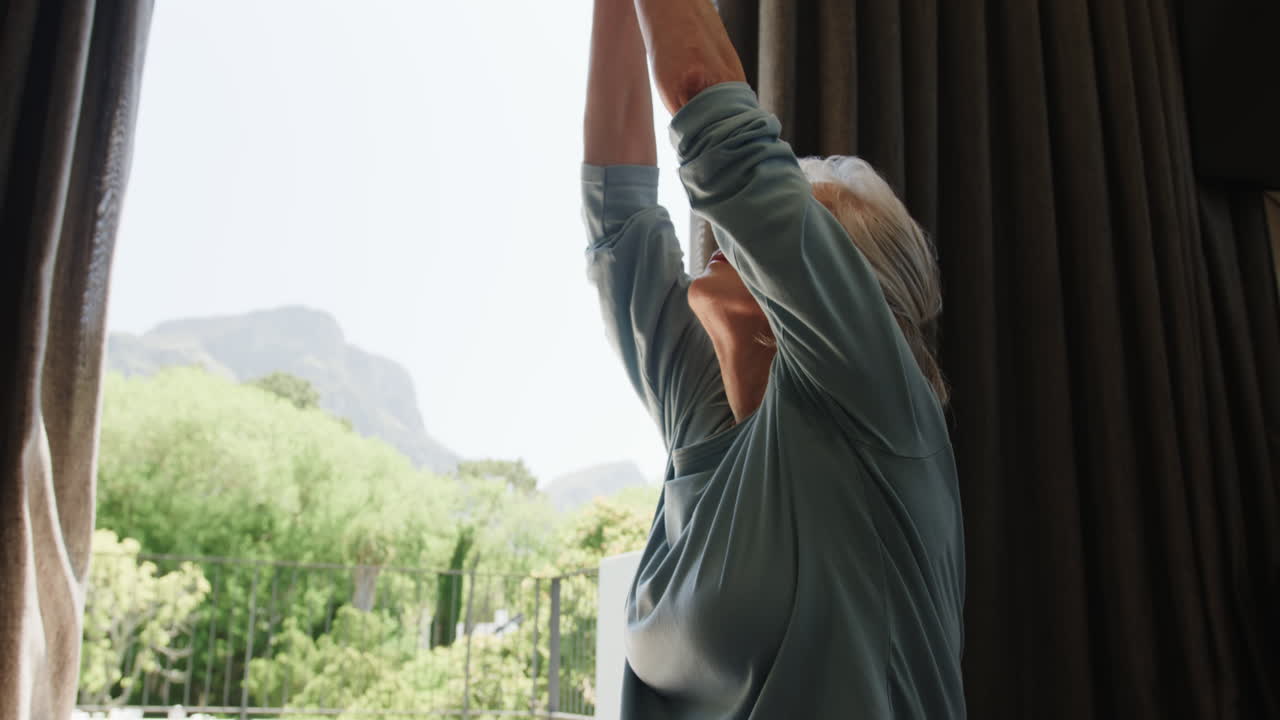 Senior woman practicing yoga at home, enjoying peaceful moment by window