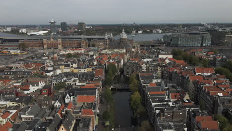 Cinematic-shot-of-The-Basilica-of-Saint-Nicholas-with-buildings-and-apartments-on-either-side-of-it-and-small-canal-passing-through-it-during-daytime-in-Amsterdam,-The-Netherlands