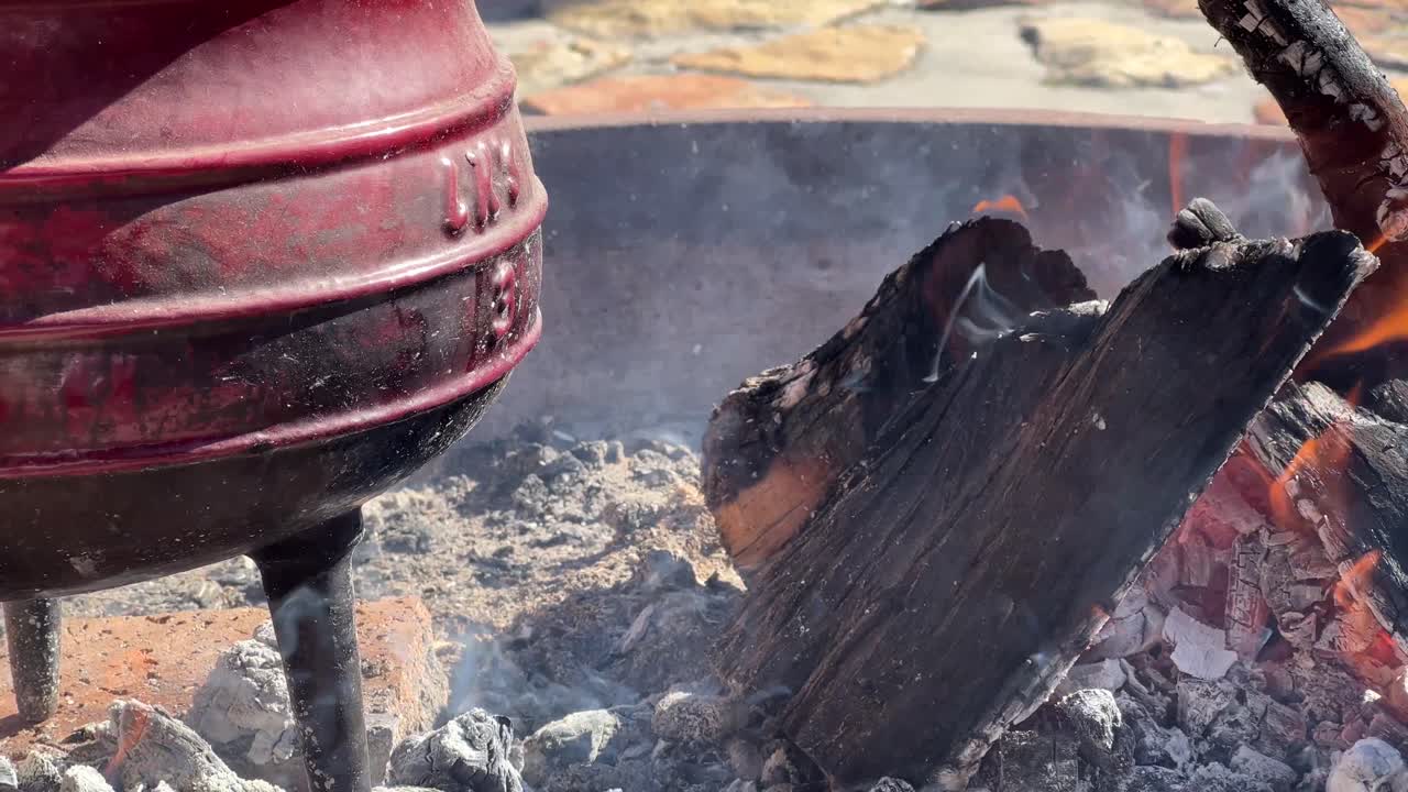 Gryte som koker over glødende kull i en bålgrube