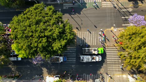 traveling left overhead aerial view of a group of garbage trucks accompanying a pilgrimage in mexico city on a sunny day, wooded area