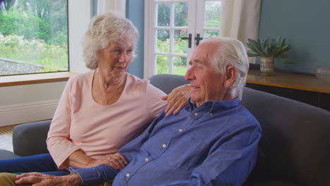 Una-Pareja-De-Ancianos-Amorosos-Disfrutando-De-Su-Jubilación-Sentados-En-Un-Sofá-En-Casa-Hablando-Y-Riendo-Juntos