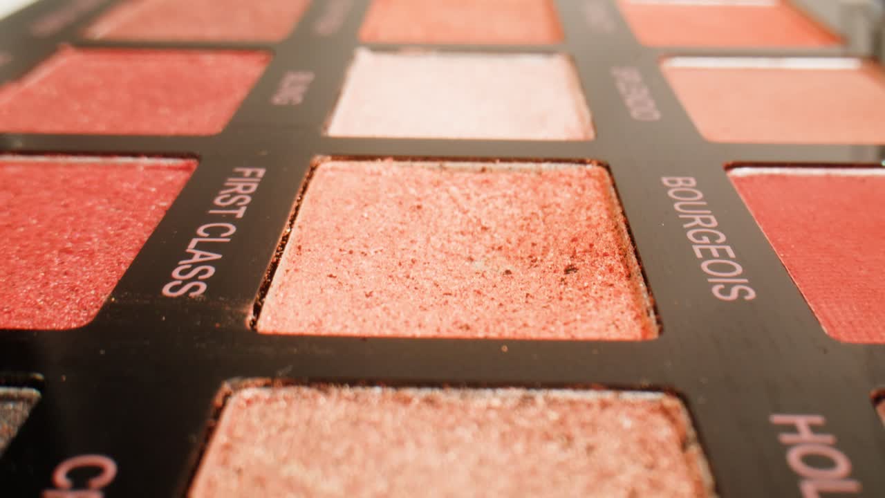 Close-up of a makeup eyeshadow palette with various shades of pink, red, and brown eyeshadows.