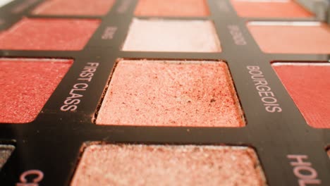 close-up of a makeup eyeshadow palette with various shades of pink, red, and brown eyeshadows.