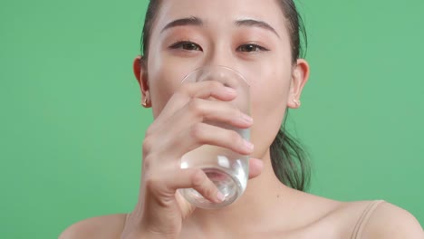 close up de una mujer asiática bebiendo agua mientras está de pie en el fondo de la pantalla verde en el estudio