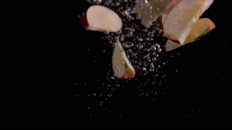 rebanadas de manzana cayendo en cámara superlenta de agua, fondo negro, muchas burbujas de aire, 4k240fps