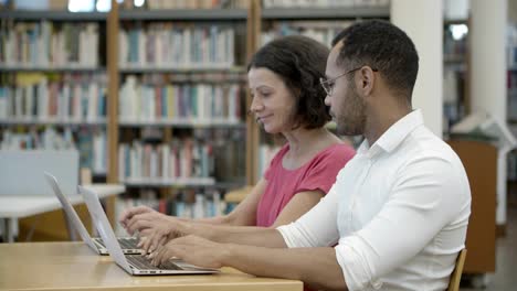 Side-view-of-colleagues-sitting-at-library-and-communicating