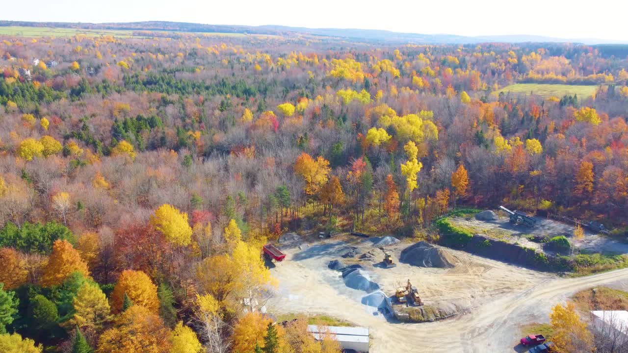 ESTRIE, QUEBEC, CANADA - DECEMBER 10, 2024: Sweeping aerial view of autumn forest with vibrant foliage surrounding a small quarry operation. Natural wilderness meets industrial activity.