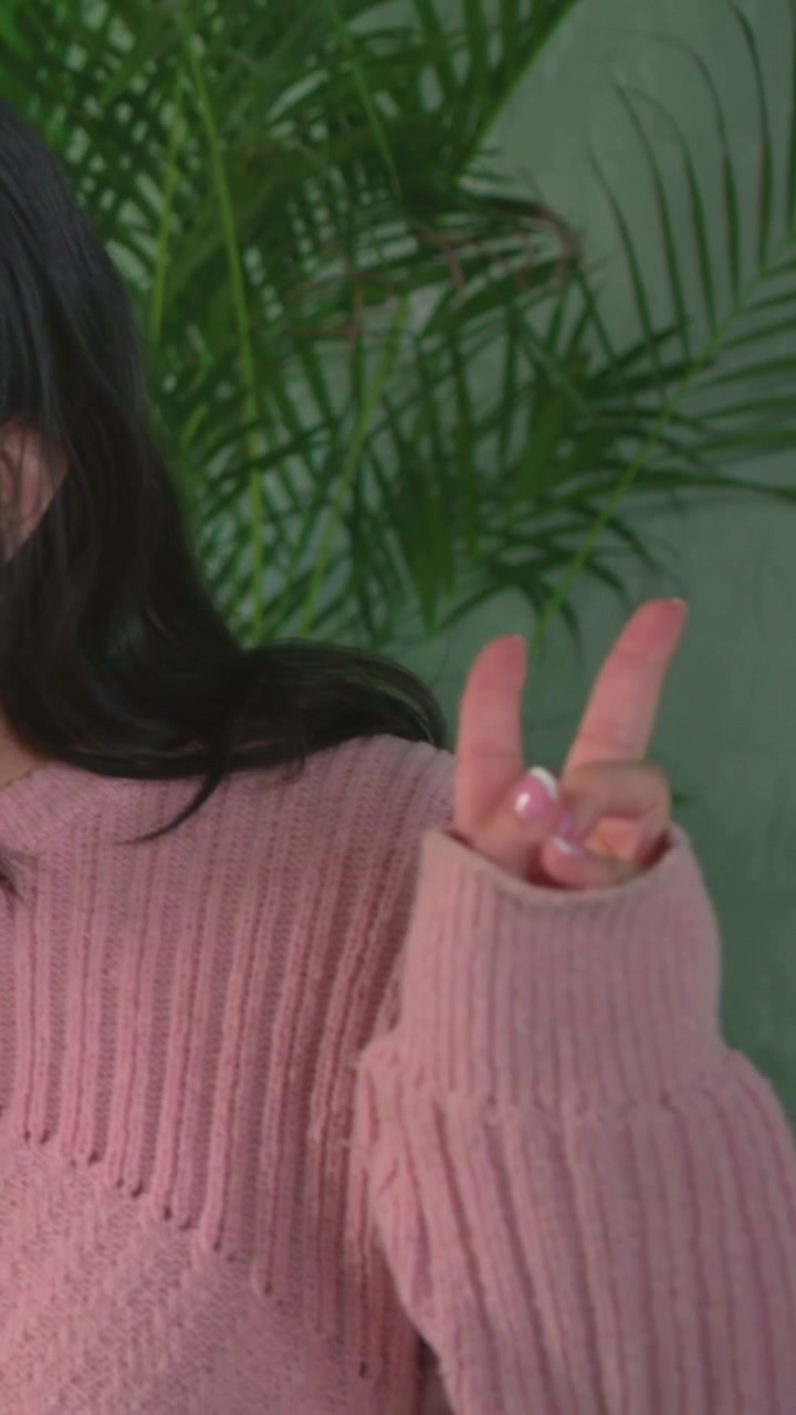 Leaning maroon-top woman leading pink-sweater woman laughing and posing in front of potted plants