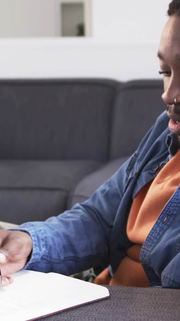 Vertikal video: Mand i orange overdel skriver i notesbog, telefon ringer, besvarer opkald, med plads til tekst.