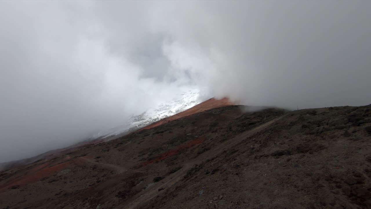 A dramatic view of Cotopaxi volcano, Ecuador, with steep slopes and heavy mist covering the peak, nature establishing as sunlight breaks between clouds on snowy ledge