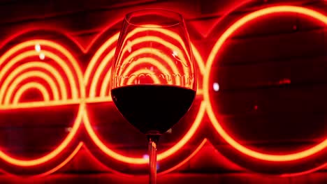 glass of red wine against neon led light on wall