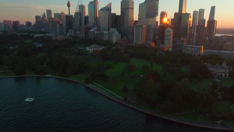 Sydney-Eye-Tower-Skyline-Der-Stadt-Royal-Botanic-Gardens-Lebhaft-Sommer-Sonnenuntergang-Australien-Luftaufnahme-Drohnenansicht-Touristenstadt-Circular-Quay-Malerischer-Hubschrauberflug-Segelboot-Fähren-Orange-Vorwärtsschwenk-Nach-Oben