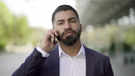 hombre de negocios serio hablando por teléfono móvil al aire libre