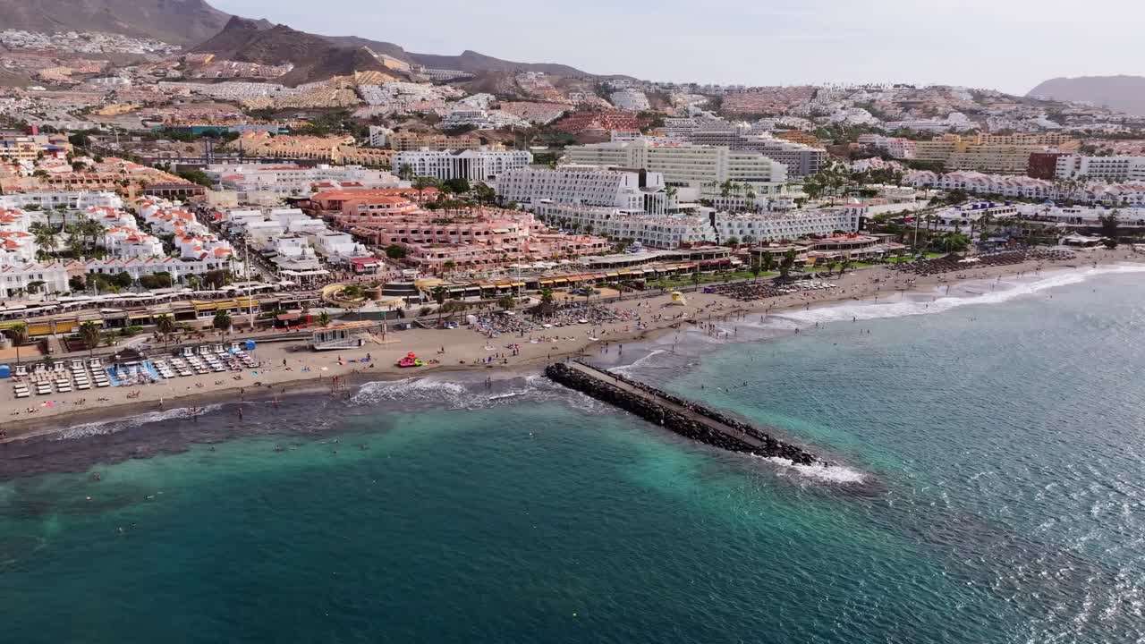 Tourists enjoy sunny Fanabe Beach as waves meet Costa Adeje’s vibrant promenade