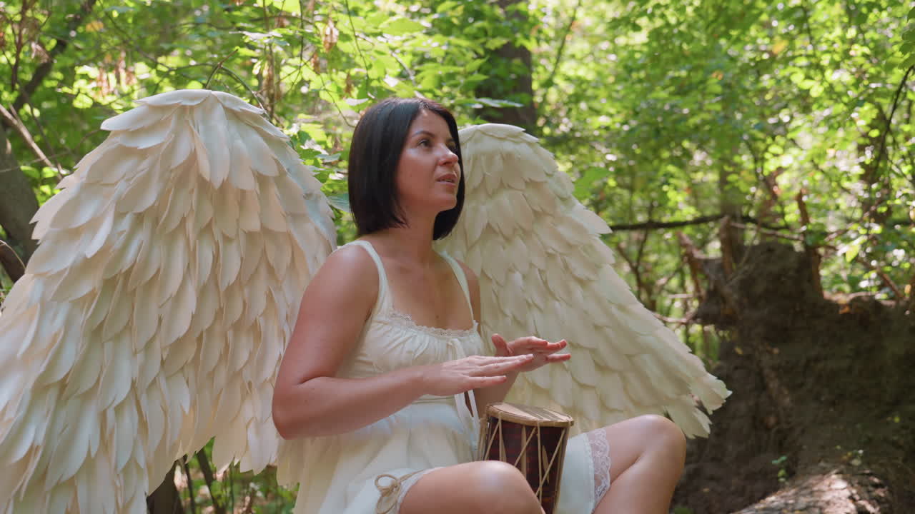 Fairy being with white wings sits in green forest beating talking drum softly, sunlight glowing through leaves as rhythmic melody forms, symbolizing harmony between sound