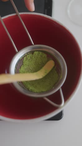 sifting matcha powder into a red bowl