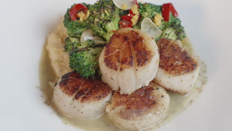 deliciosos medallones de vieiras en salsa, con una guarnición de polenta y cubiertos con brócoli, en un tiro giratorio