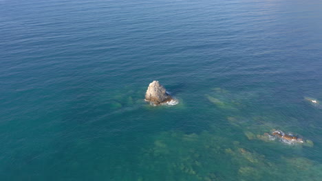 Aéreo:-Toma-Panorámica-Lenta-De-Una-Gran-Roca-En-Medio-Del-Mar-Azul,-Claro-Y-Tranquilo