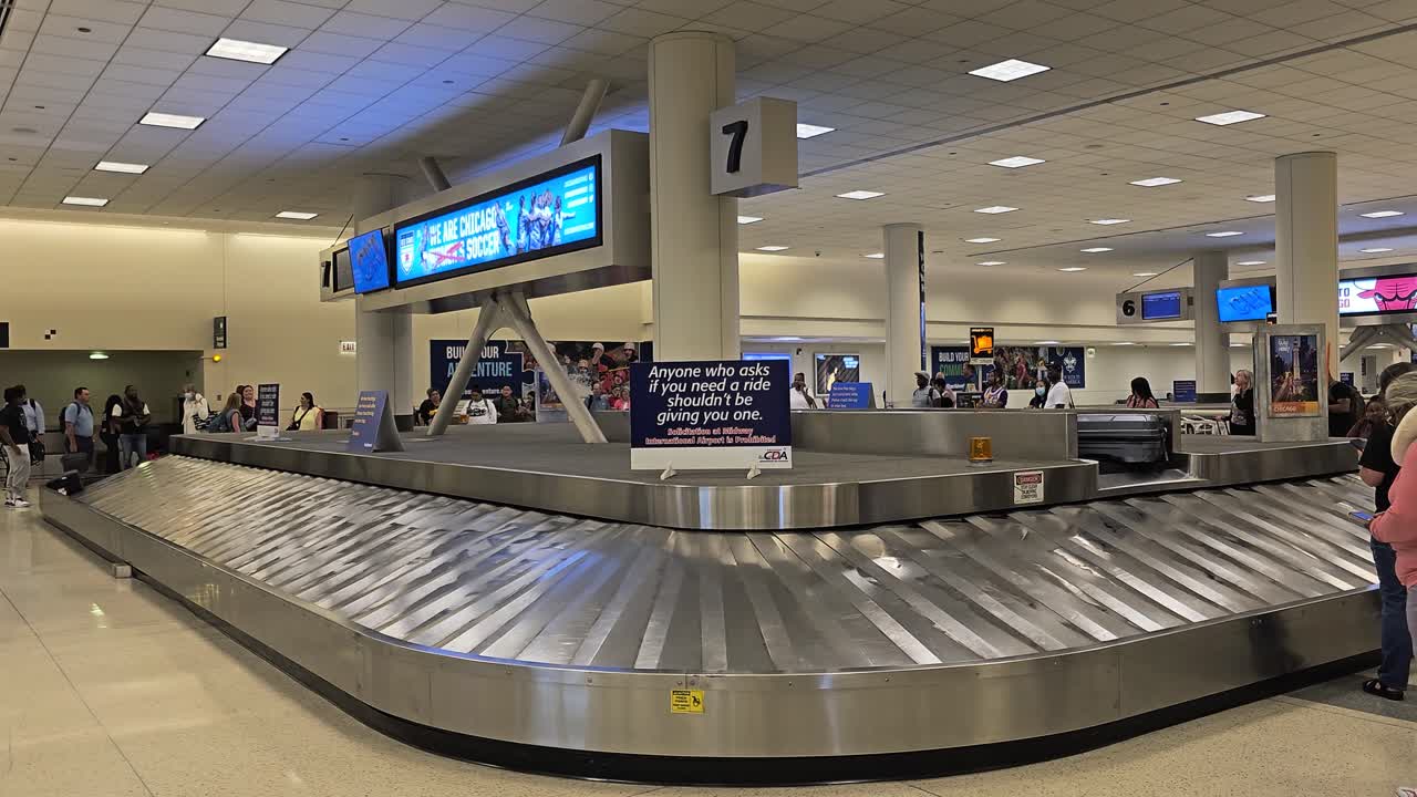 passengers waiting at spinning bag claim with luggage dropping at Chicago Midway International Airport