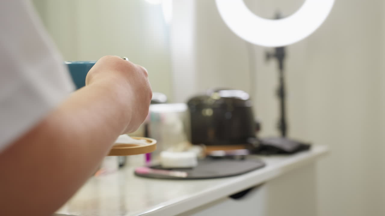 Beautician carefully holds tea cup on small tray while approaching client in salon, ring light glowing in background, creating calm and professional atmosphere focused on comfort and attentive service