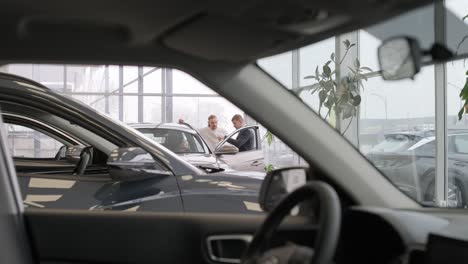 un joven vendedor de coches mostrando a una pareja de jóvenes un nuevo automóvil en el salón de concesionarios.